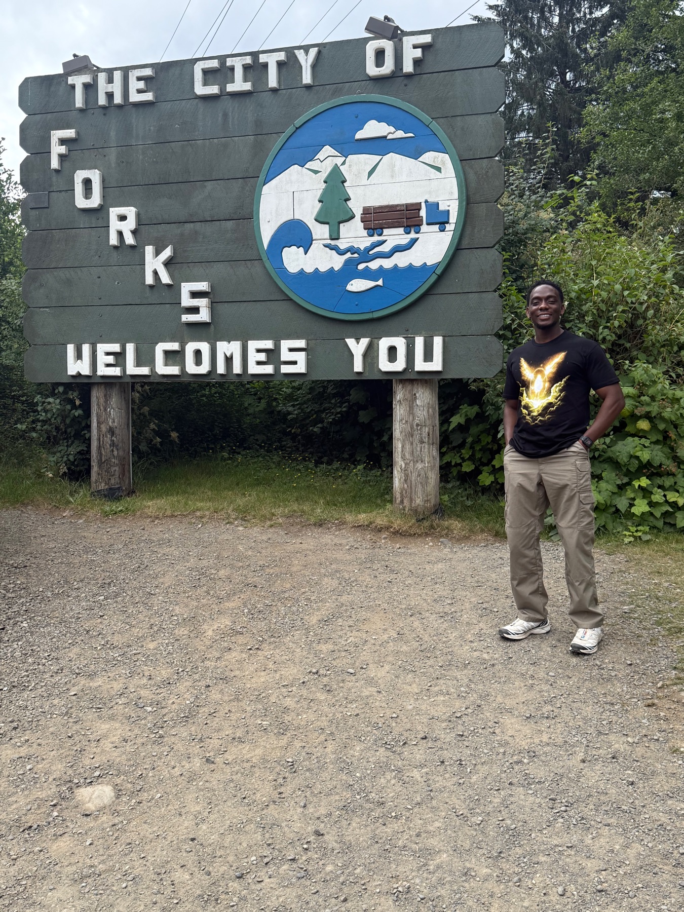 Standing at the weathered The City of Forks Welcomes You sign on the edge of town